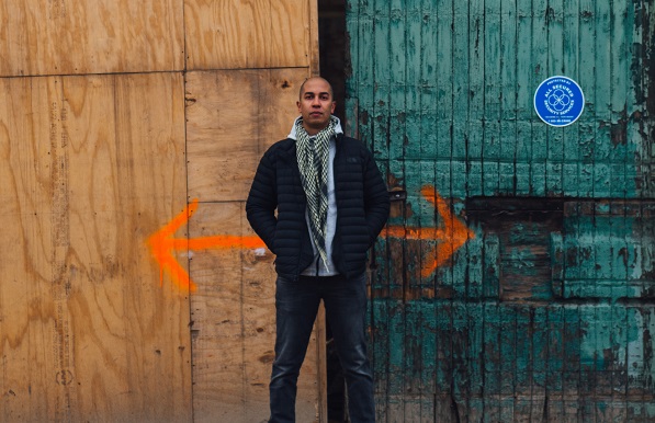 student against wall with detour arrows painted on it behind him