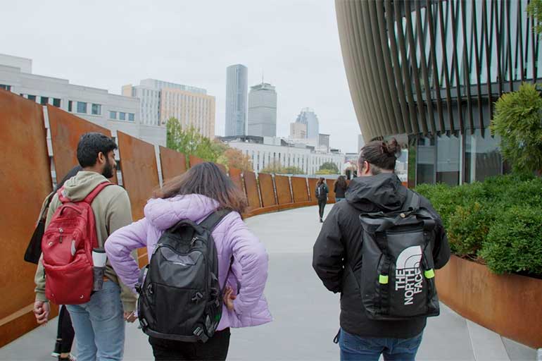 students walking on campus with Boston skyline shown