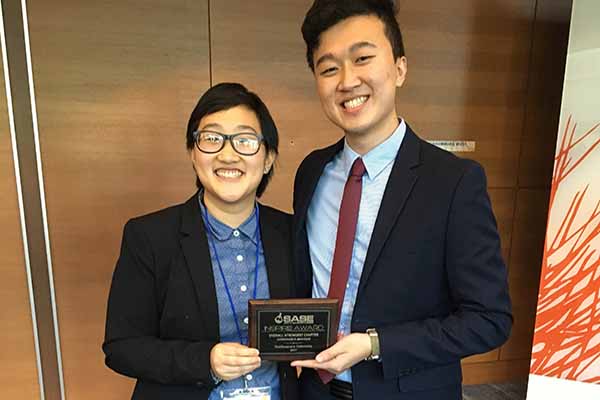 two Asian students with award plaque in hands smiling