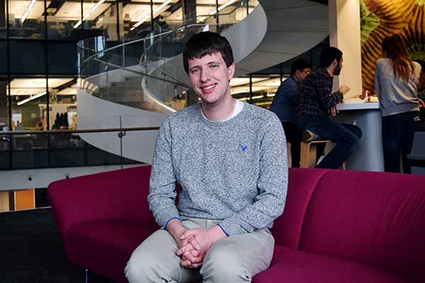 student sitting on red chair posing with spiral stairs in background