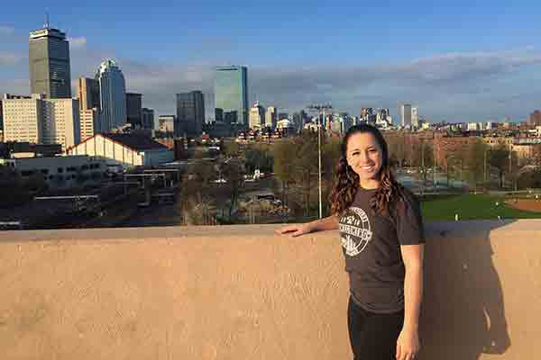 student posing with Boston skyline in background