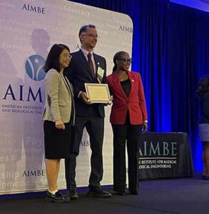 professor joy on stage at AIMBE conference holding plaque