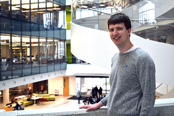 student posing with background showing inside of ISEC with glass walls and spiraling staircase