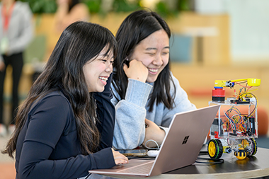 students smiling looking at a computer that is connected to a robot
