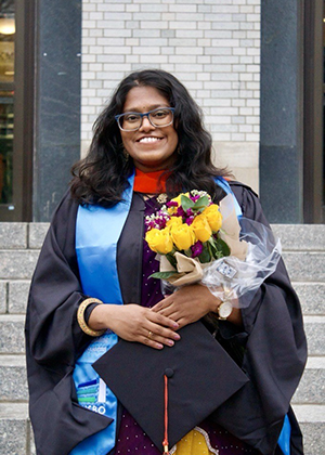 sowdamini ponnada standing in her graduation attire holding flowers
