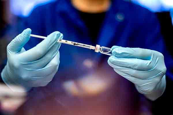 medical worker putting needle in vaccination container