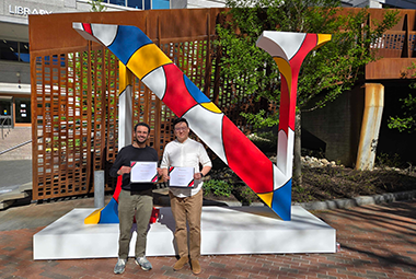 Bishoy Galoaa and coworker standing in front of an enlarged northeastern N