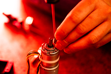 red tinted image of a hand working on a robot 