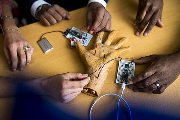 The hands of Stella Banou, Kaushik R. Chowdhury and William J. Tomlinson surround a robotic hand attached to circuits via wires.