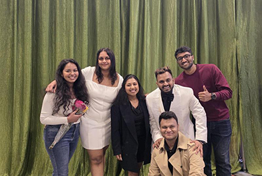 six people stand in a group in front of a green backdrop