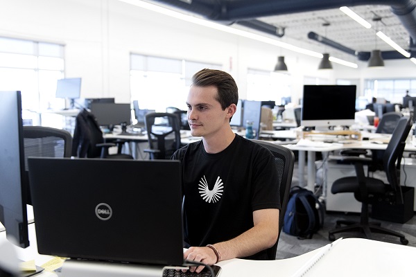 Northeastern student Alex Bender works on a Dell laptop in the sunlit offices of Boom Supersonic.