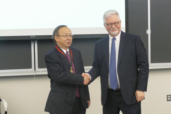 provost shakes hands with guest who has medal around neck