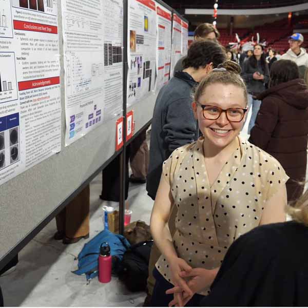 student in front of research poster at expo