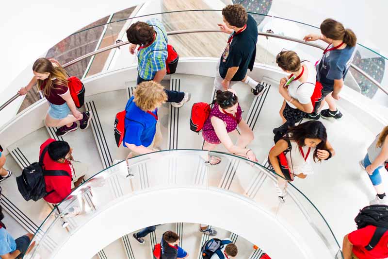 students with red bags walking together down spiral staircase
